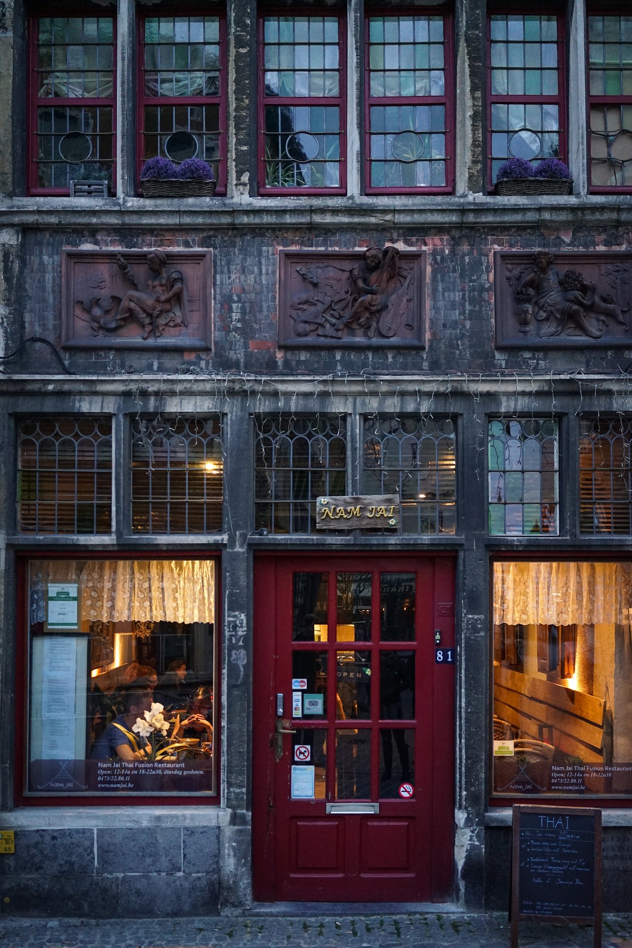 A Thai restaurant with a red door and large windows, where people are dining inside under warm lighting.
