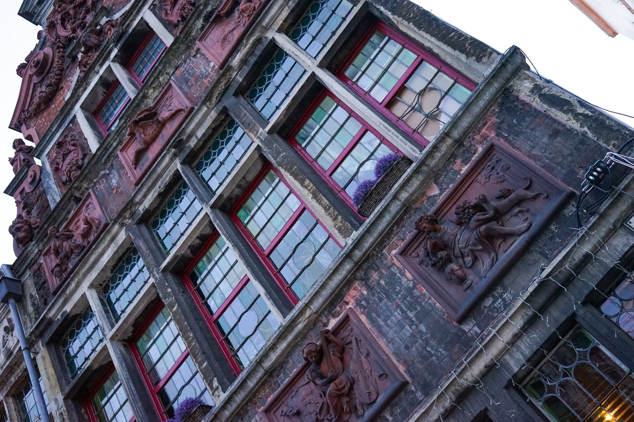 A historic brick building in Ghent with red-framed windows, decorative sculptures, and flower boxes on the facade.