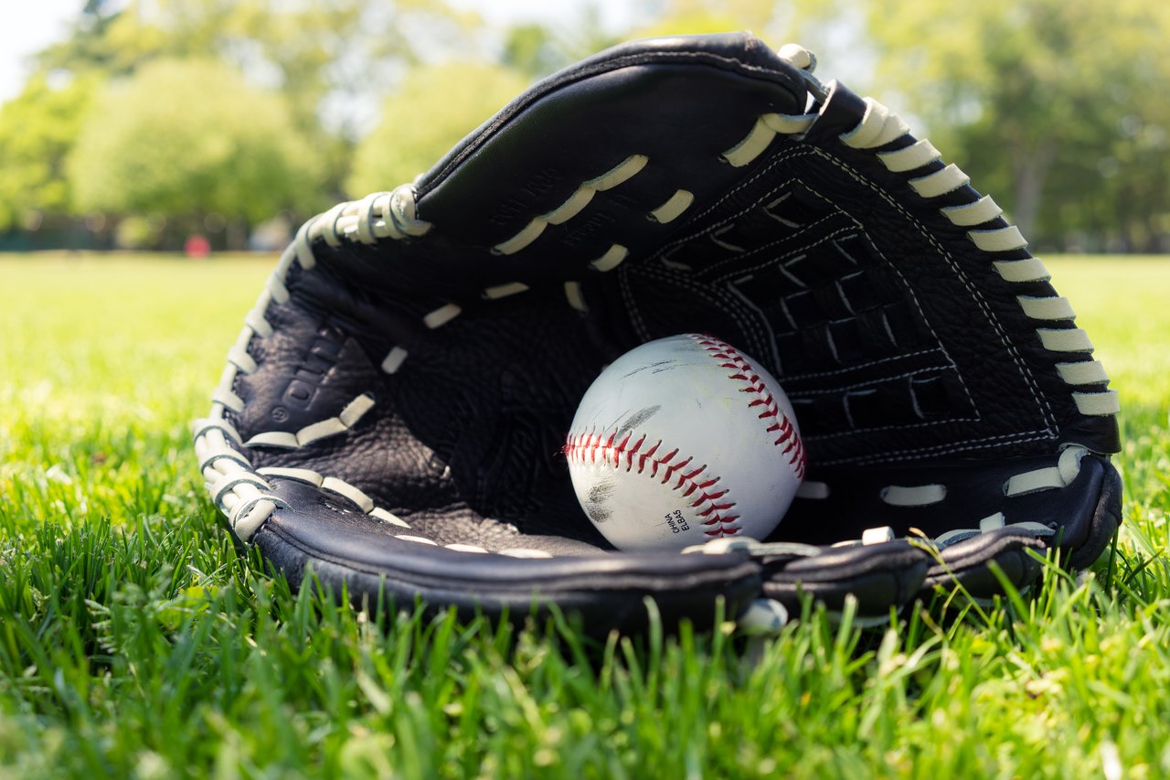 A baseball rests inside an open black glove on the grass in a park.