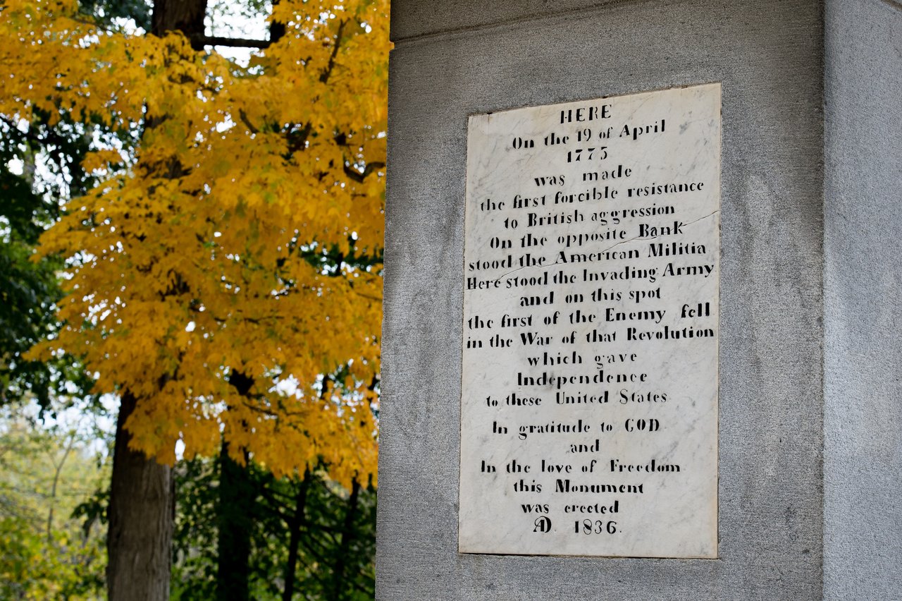 A historical plaque on a stone monument marks the site of the first armed resistance in the American Revolution.