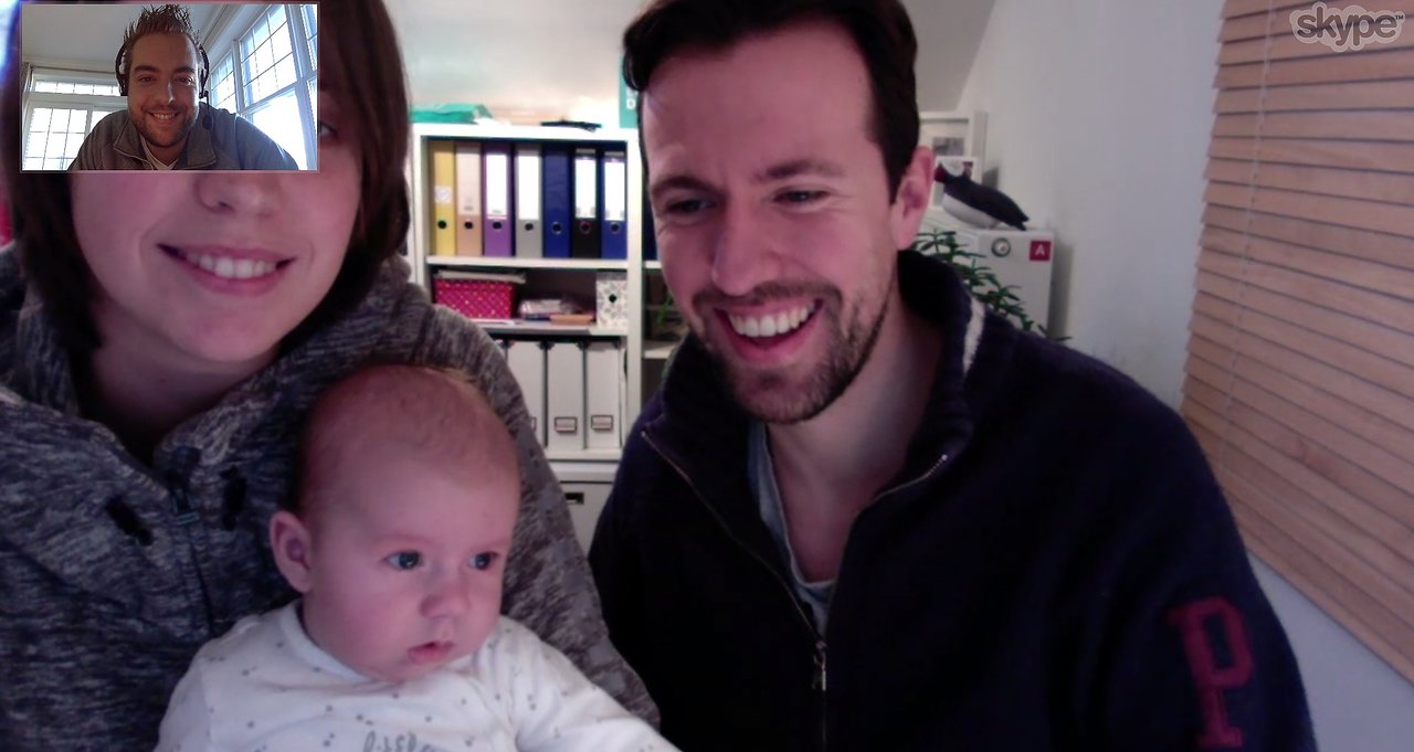 A baby has their first Skype call with a smiling family and a person on the video chat screen.