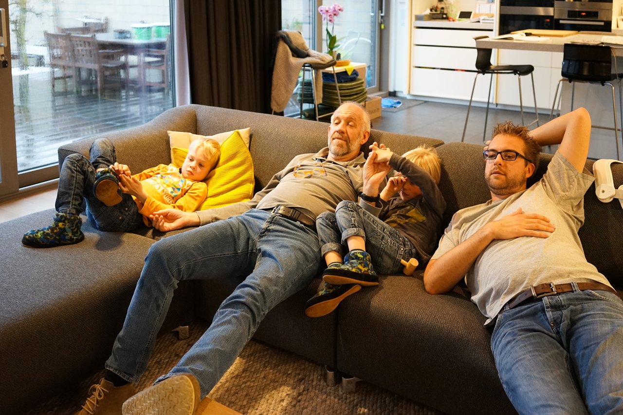 Three generations relax on a couch; two children play while two adults rest in a cozy living room.