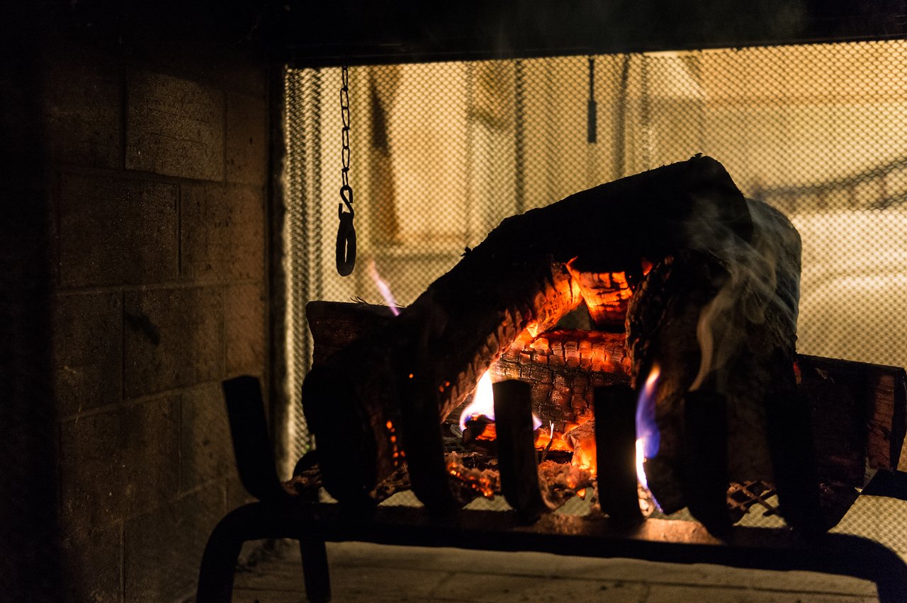 A fireplace with burning logs and glowing embers, with a metal screen in the background.