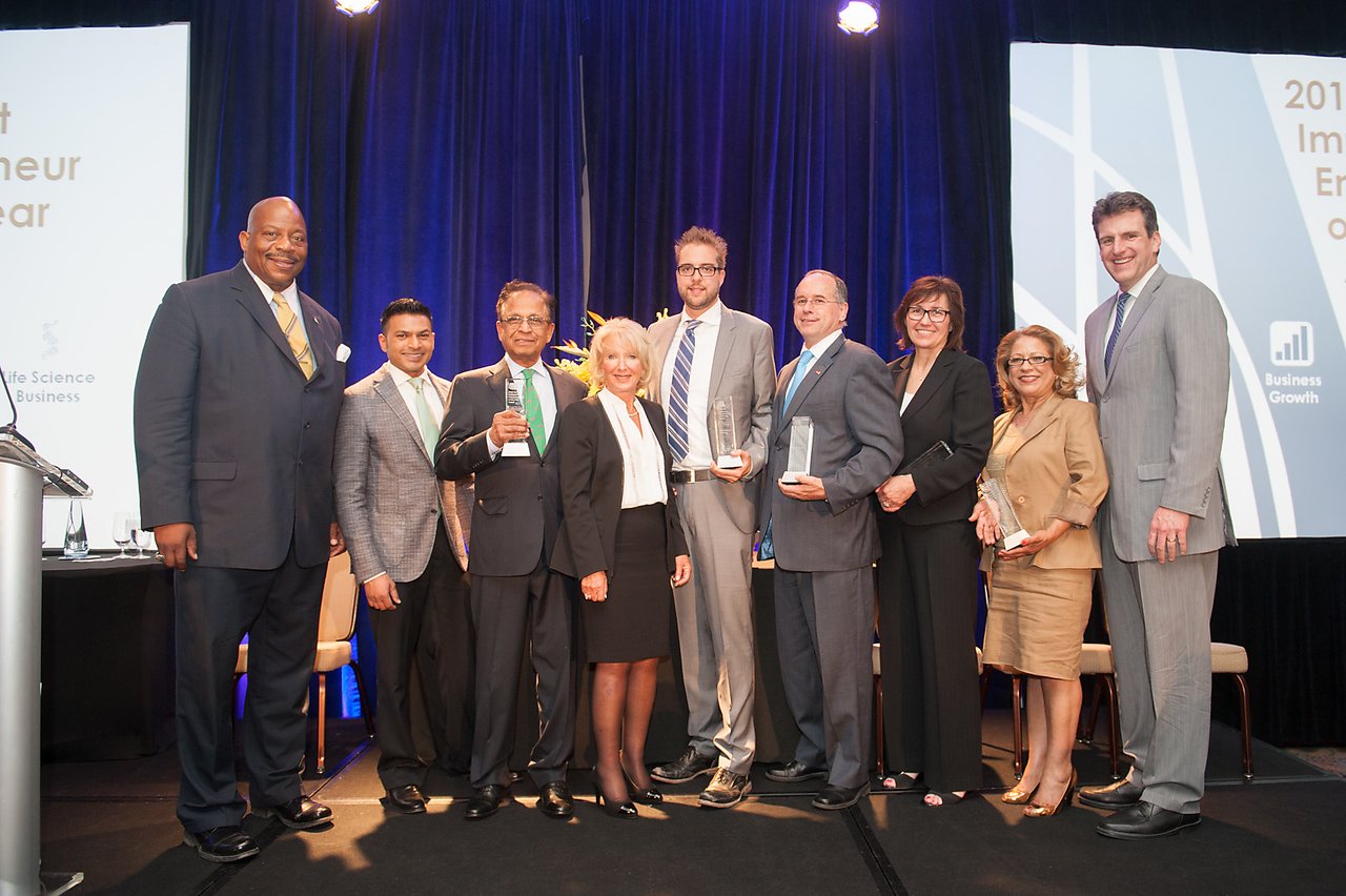 A group of award winners stands on stage, holding trophies and smiling for a photo at a formal event.