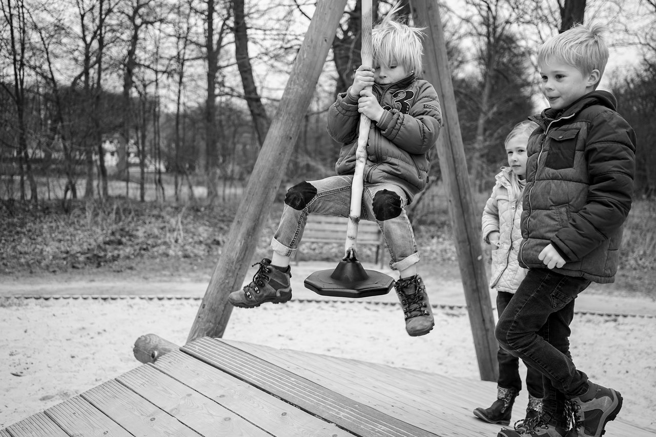 A child rides a zipline at a playground while two other children watch nearby.