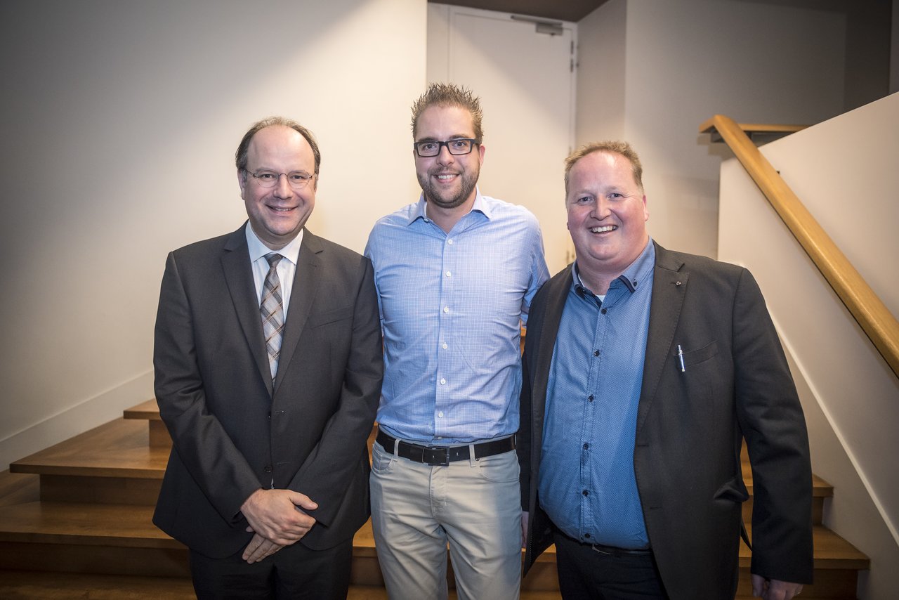Three men stand together, smiling at the camera, during a presentation event at Antwerp University.