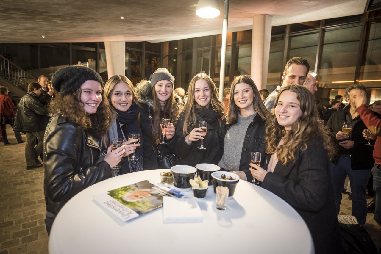 A group of young people smiles and holds drinks around a table at a university event in Antwerp.