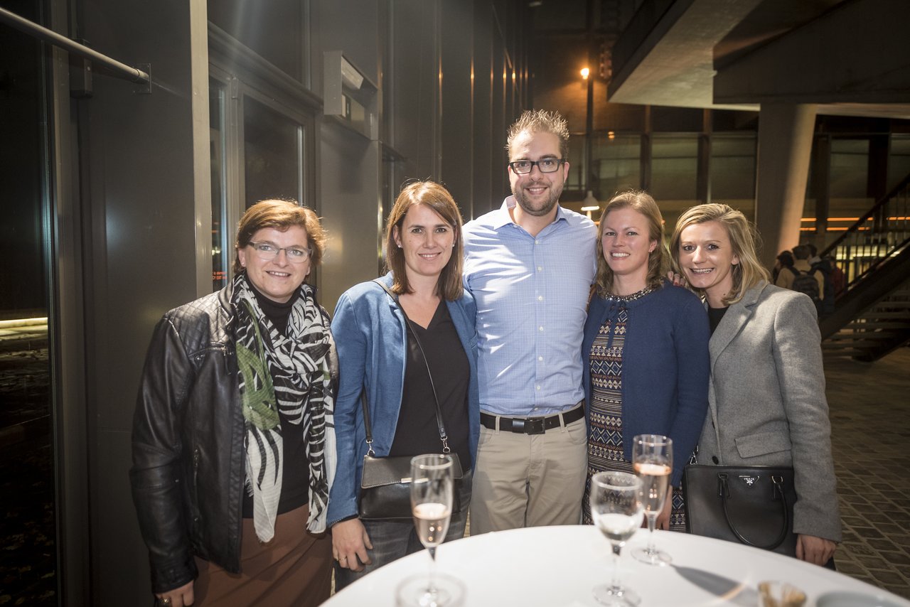 A group of five friends posing together at an event, smiling and holding drinks.