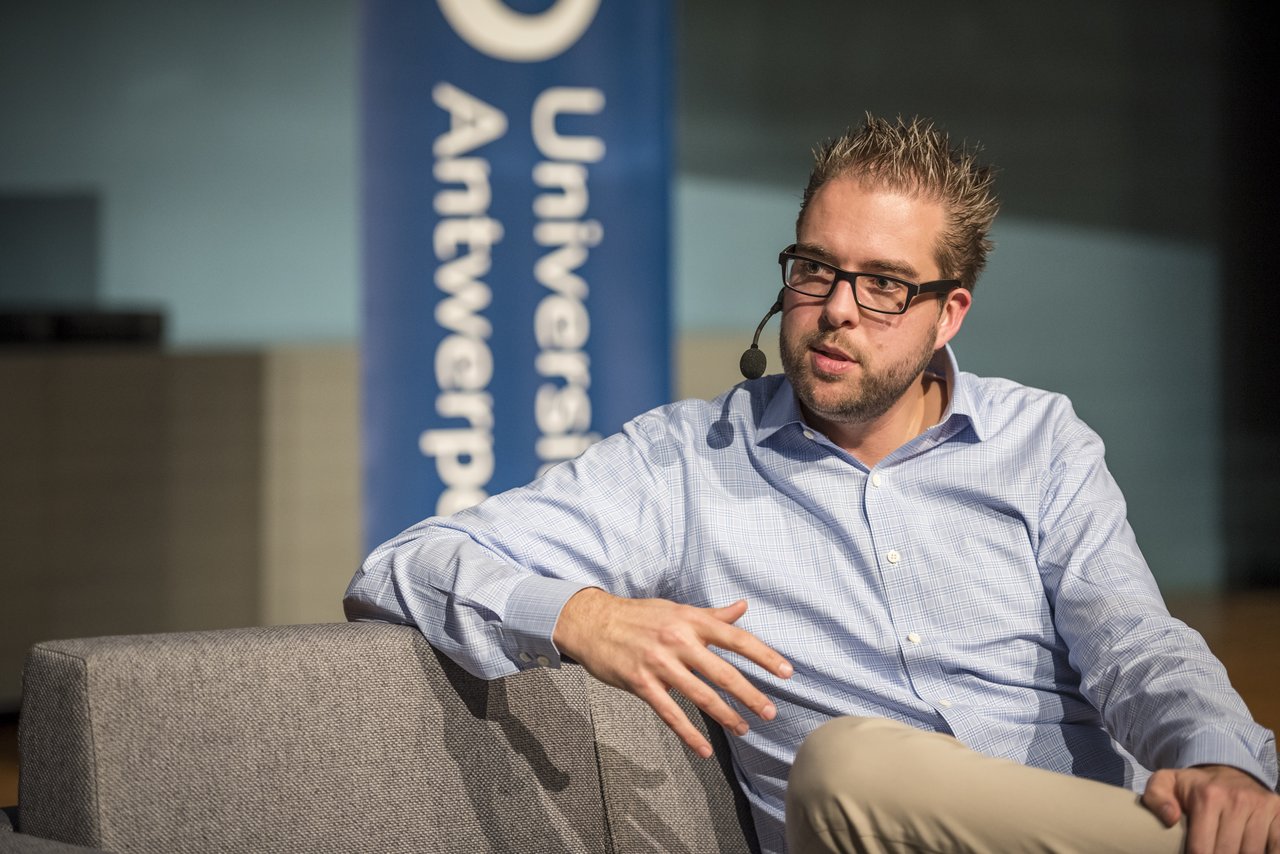 A man wearing a headset microphone speaks while seated during a presentation at the University of Antwerp.