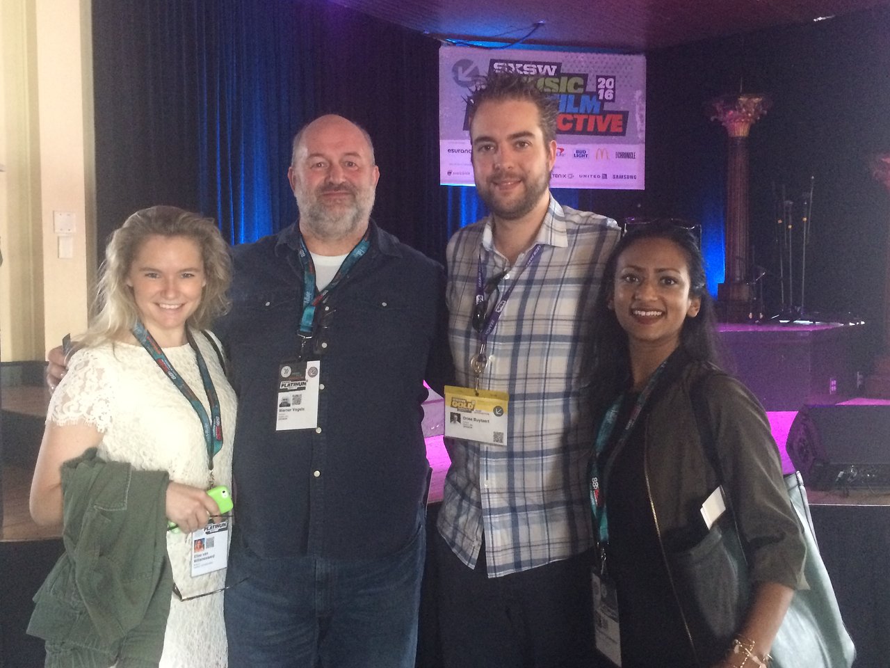 Four people posing together at a conference, all wearing event badges and smiling at the camera.