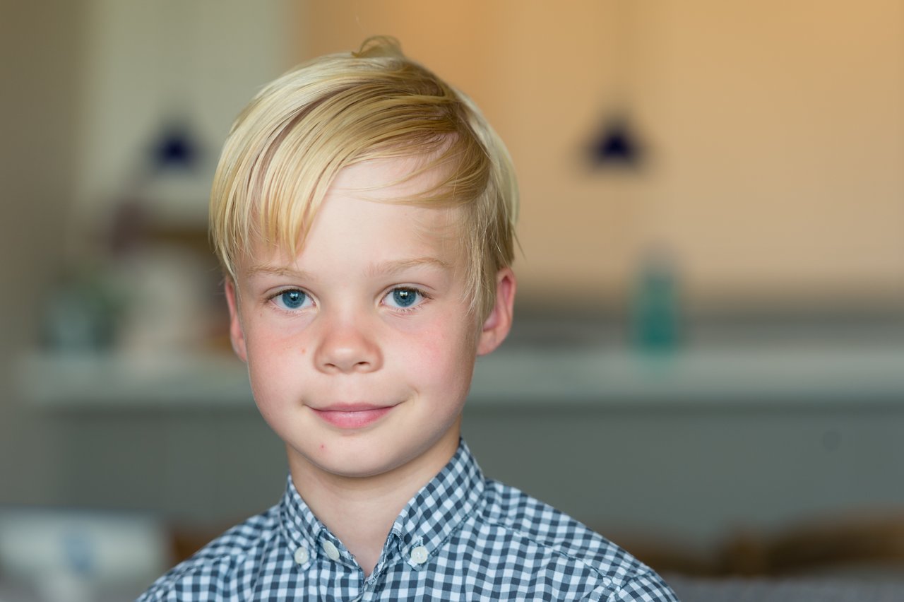 A young boy with neatly styled blonde hair smiles slightly while looking directly at the camera.