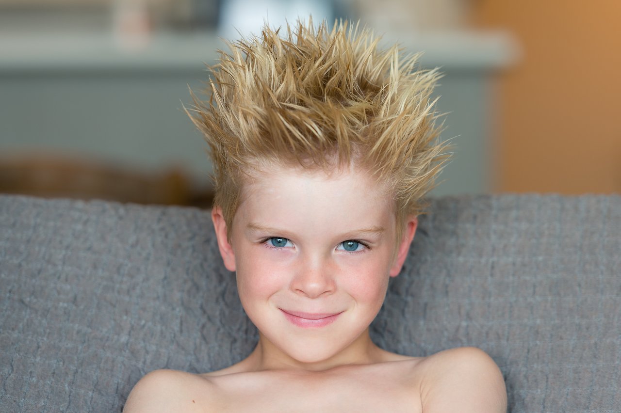 A smiling child with spiky, gelled hair sits on a couch, looking directly at the camera.