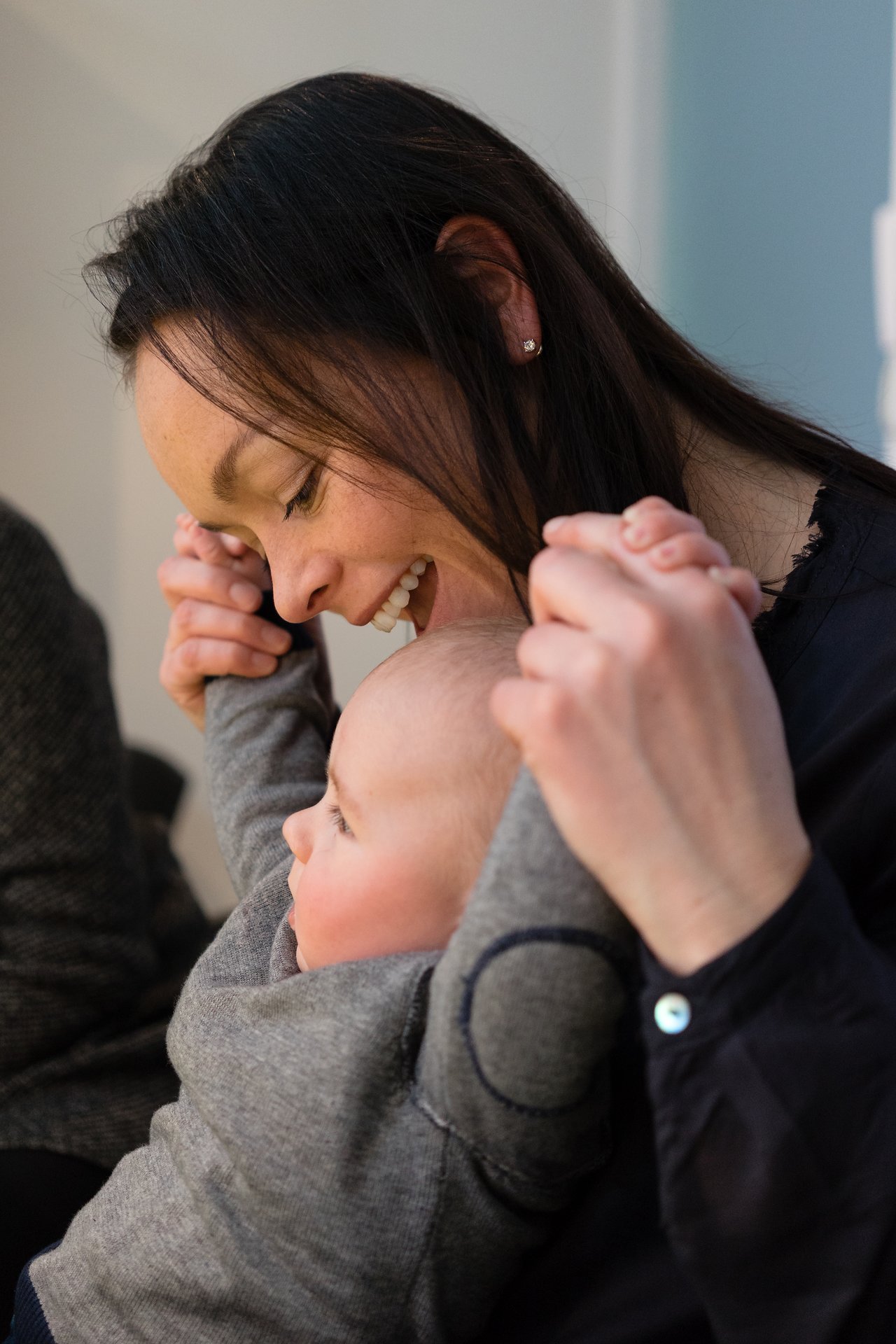 A woman smiles while holding a baby's hands, lifting them up playfully.
