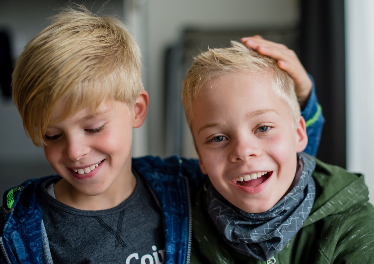 Two smiling boys are playfully posing together, one placing his hand on the other's head.