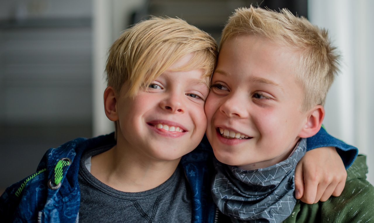 Two smiling boys with arms around each other, laughing and having fun together indoors.