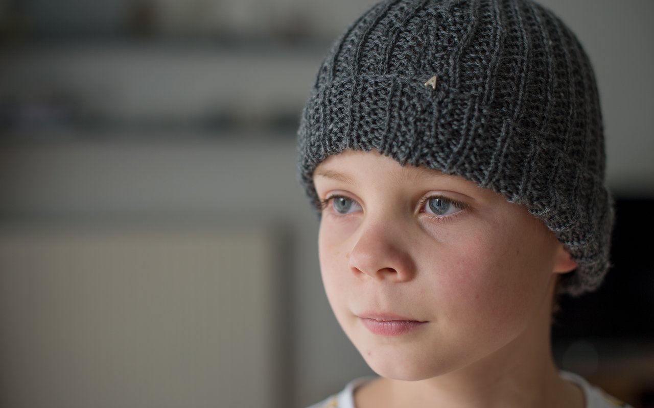A child wearing a gray knitted hat looks off to the side with a neutral expression.