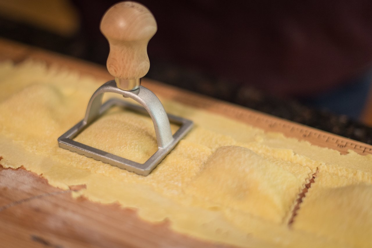 A ravioli cutter presses into fresh pasta dough, shaping homemade butternut squash ravioli on a wooden surface.
