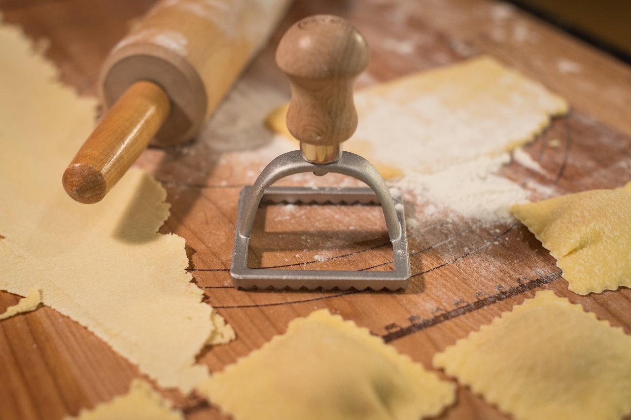 A ravioli cutter and rolling pin on a floured wooden surface with freshly made butternut squash ravioli.