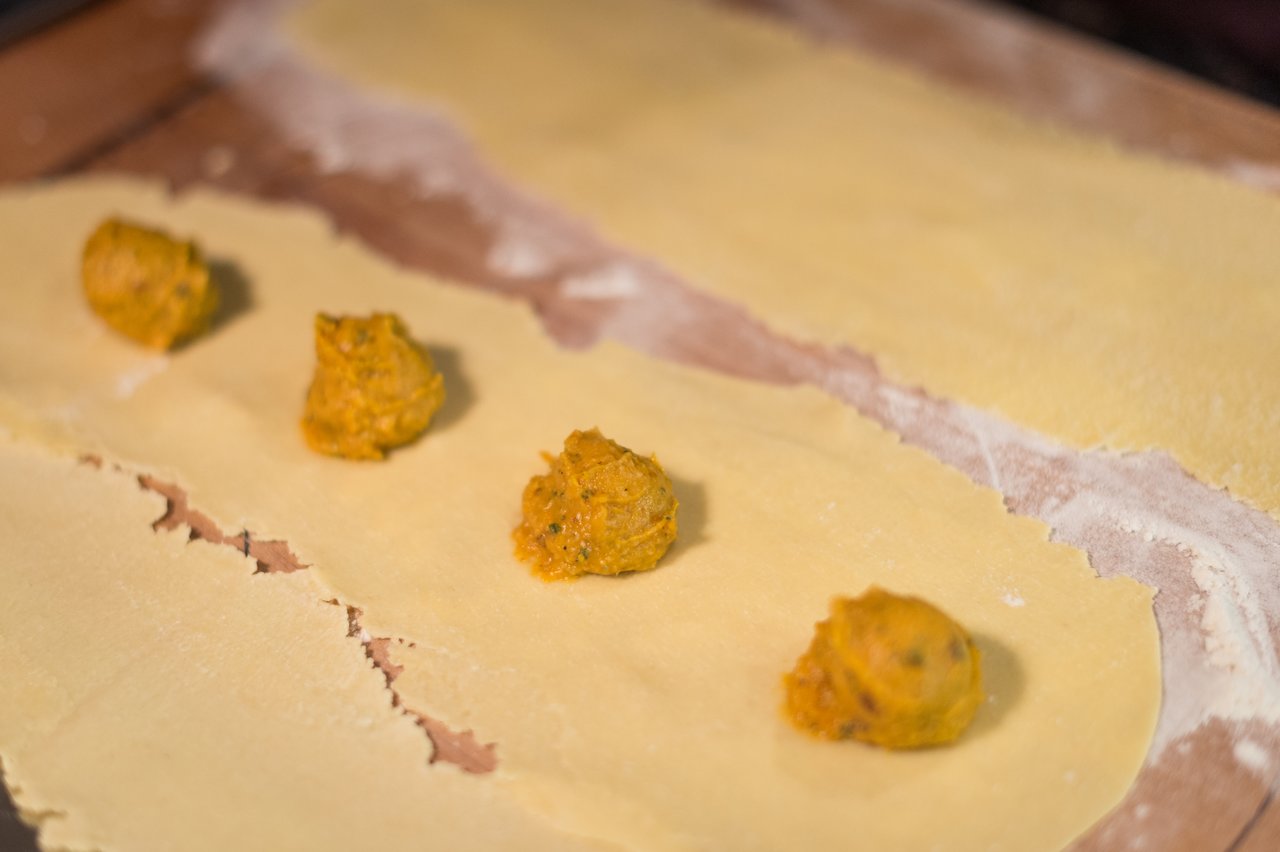 Fresh pasta sheets with scoops of butternut squash filling, prepared for making homemade ravioli.