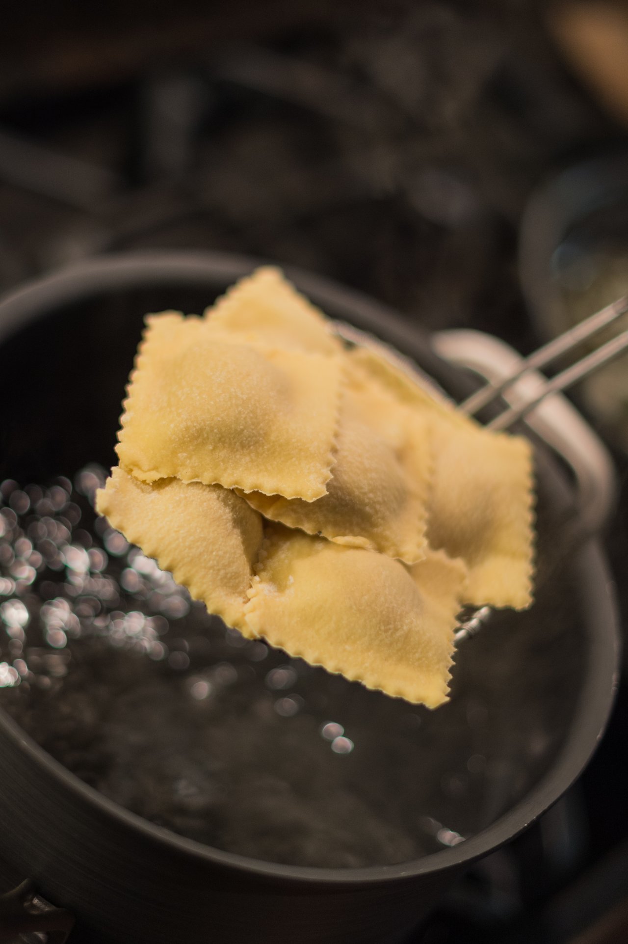 Freshly cooked butternut squash ravioli being lifted from a pot of boiling water with a slotted spoon.