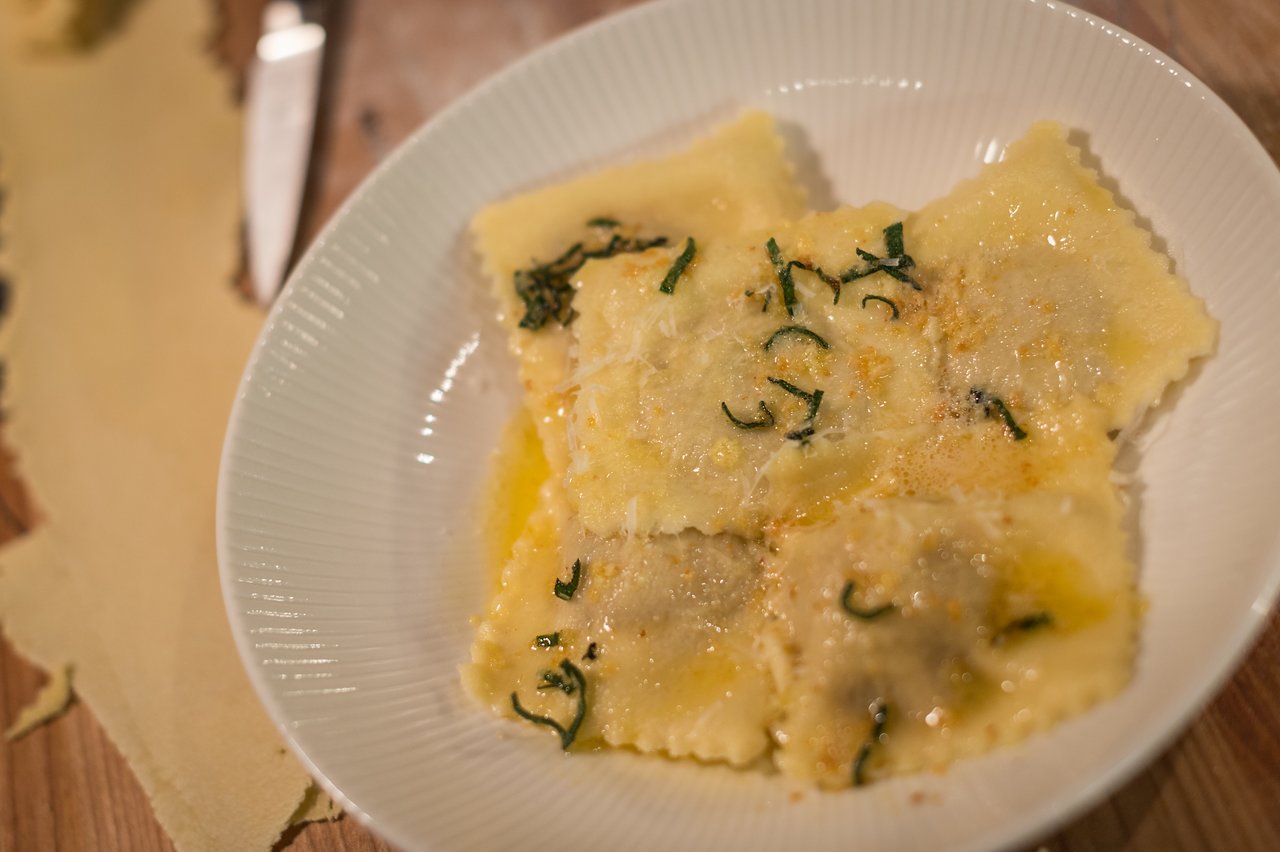 A plate of homemade butternut squash ravioli topped with butter, herbs, and grated cheese on a wooden surface.