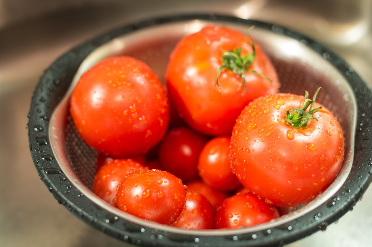 A colander filled with freshly washed red tomatoes, with water droplets visible on their surface.