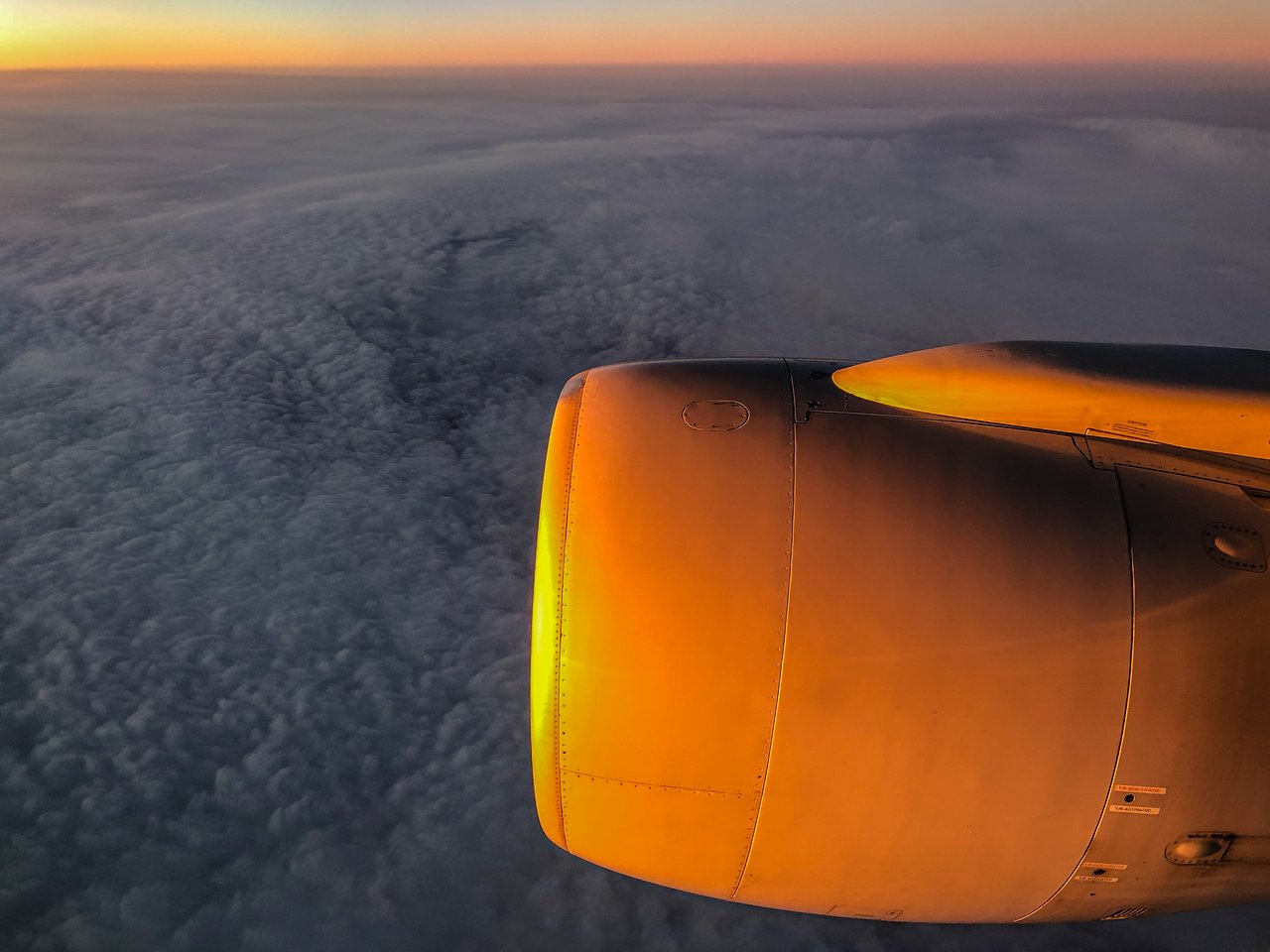 Airplane engine reflecting warm sunlight with clouds below and a colorful sky in the background.