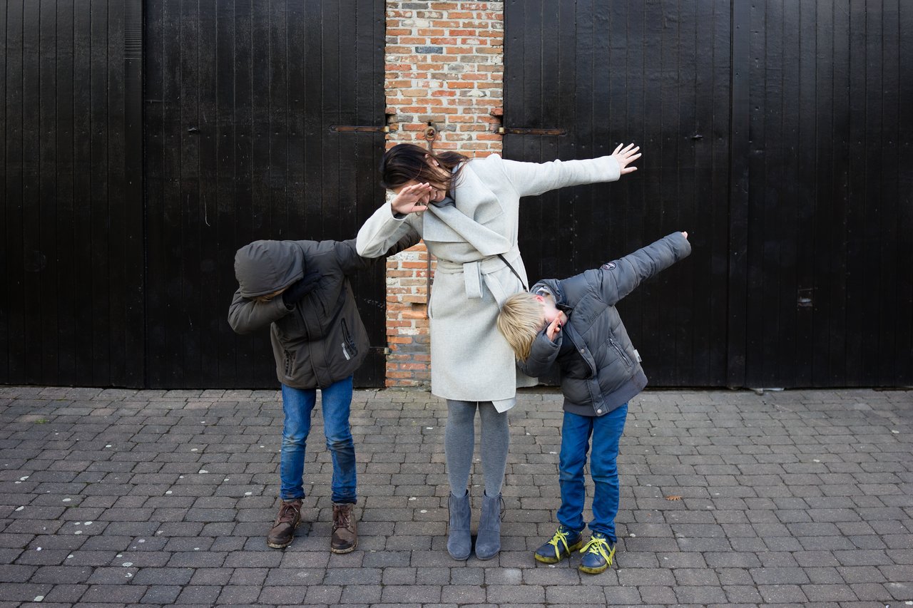 A woman and two children perform the dab pose, tilting their heads into their arms with arms extended outward.
