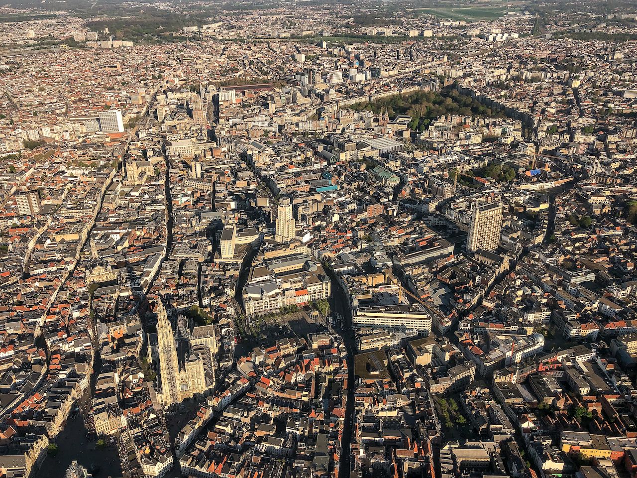 Aerial view of Antwerp, Belgium, showing dense city buildings, streets, and the Cathedral of Our Lady in sunlight.
