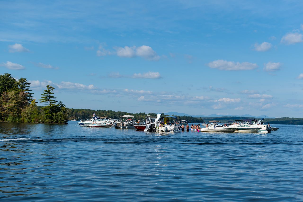 People gather in the water near several boats on a lake under a clear sky.
