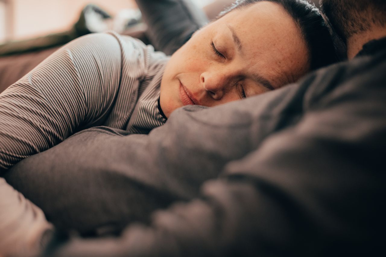 A woman with closed eyes rests her head on someone's chest, appearing to be napping.