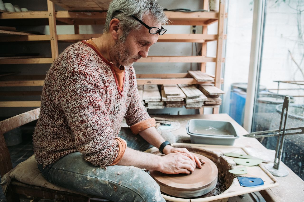 A man shapes clay on a spinning pottery wheel in a ceramics workshop.