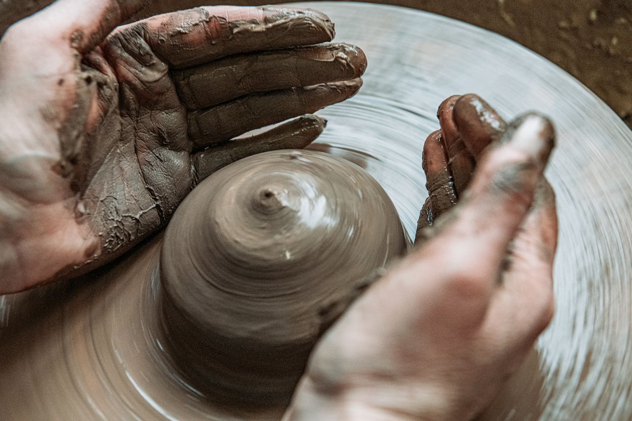 Hands covered in wet clay shape a spinning pottery piece on a wheel.