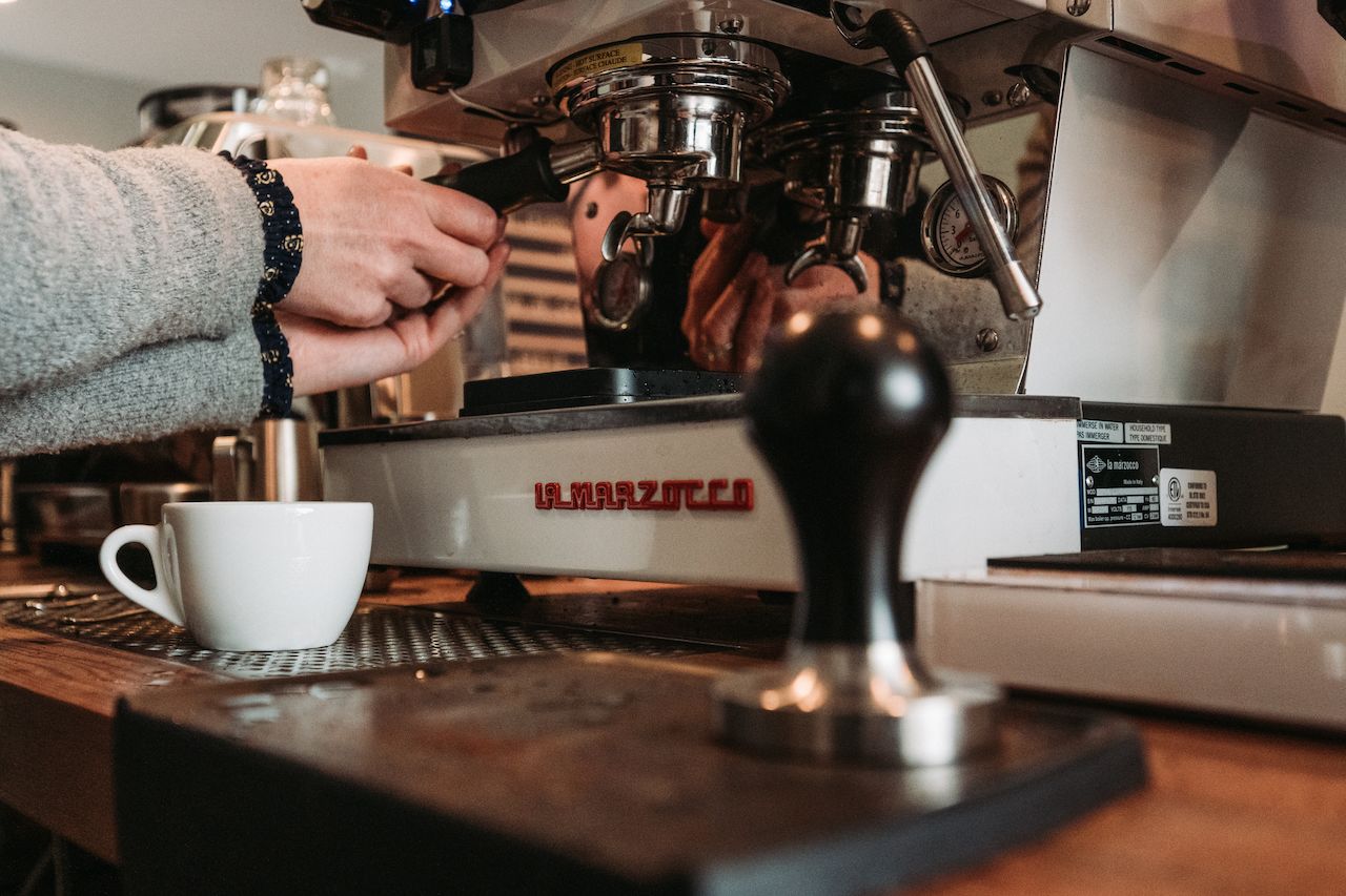 A person adjusts a portafilter on an espresso machine during a barista training class, with a cup nearby.
