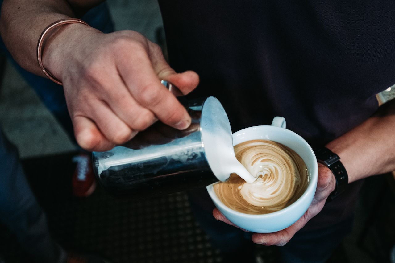A person pours steamed milk into a cup of coffee, creating latte art during a barista class.
