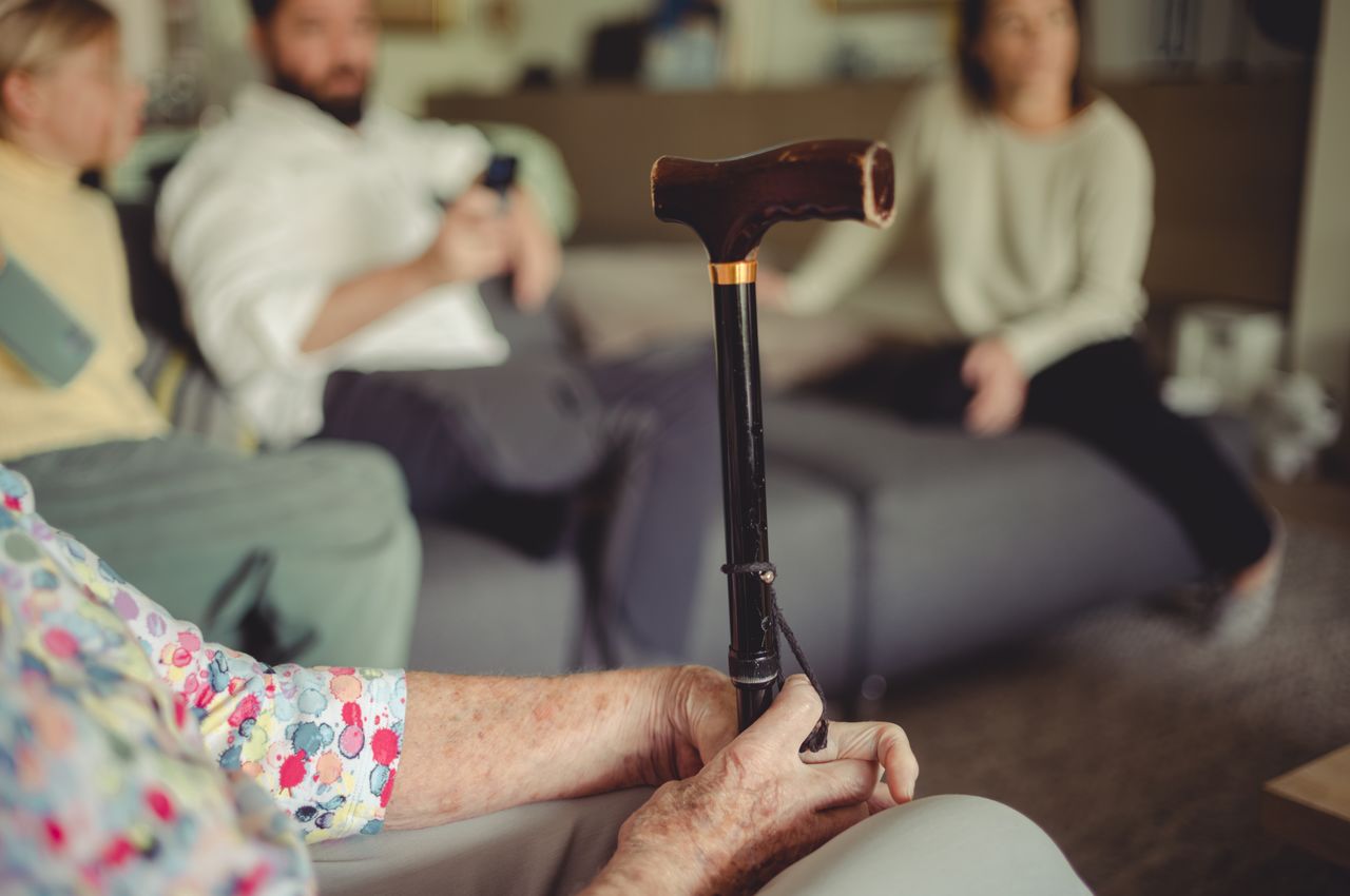 A women holding a cane while sitting on the coach.