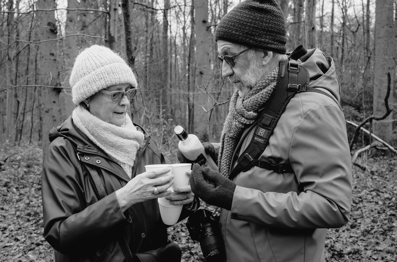A man and woman standing in the woods pouring a drink.