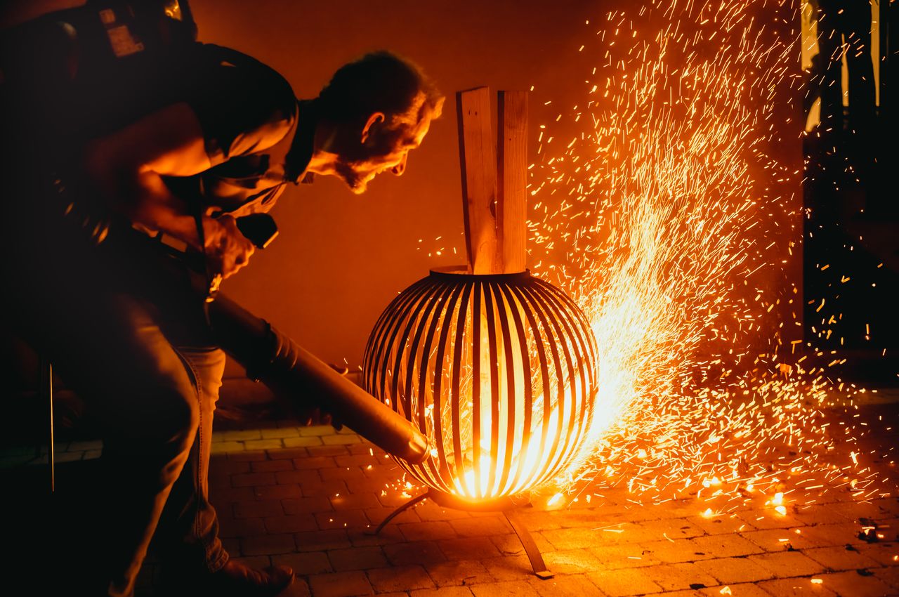 Thousands of embers dance in the air as a person uses a leaf blower to fan the flames of a fire pit.