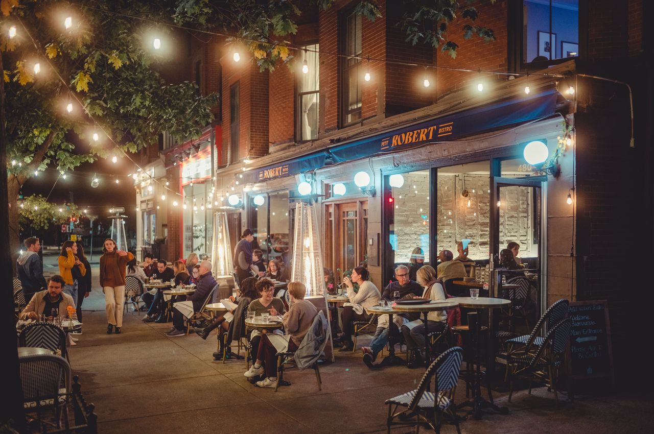 People dining on the sidewalk, seated on small French tables.