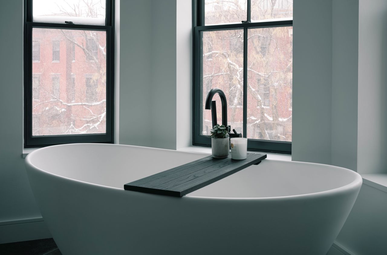 A white bathtub with a black ledge and a window above it.