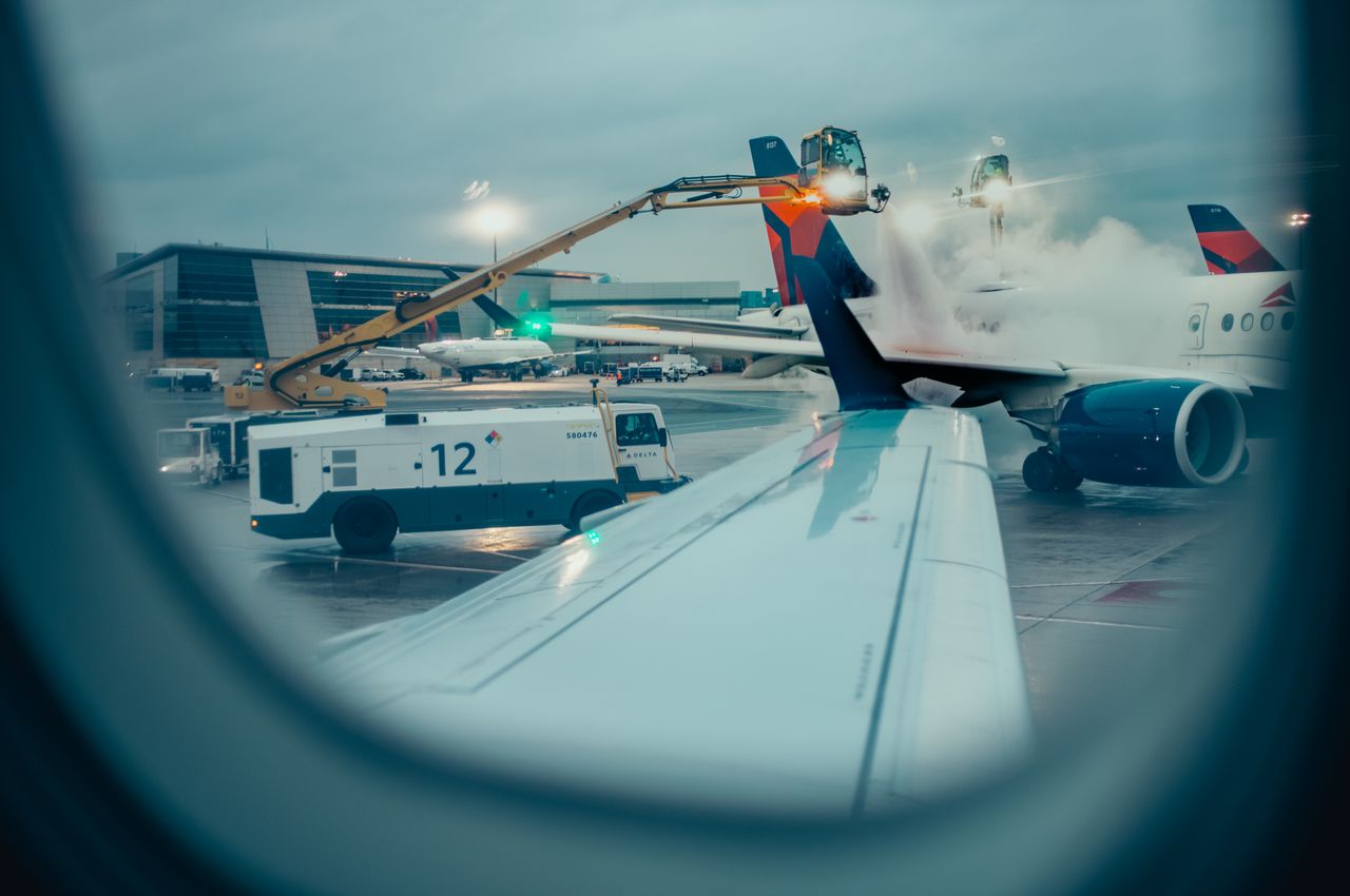 The view from an airplane window shows another plane being de-iced, fluids sprayed on the wing to remove any ice and snow.