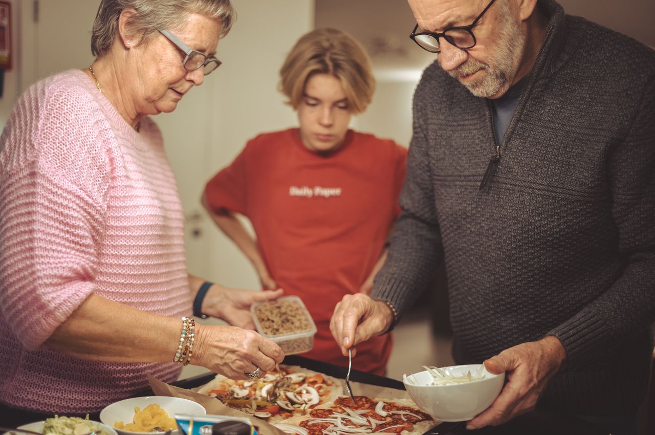 Two adults preparing a pizza while a young boy watches.