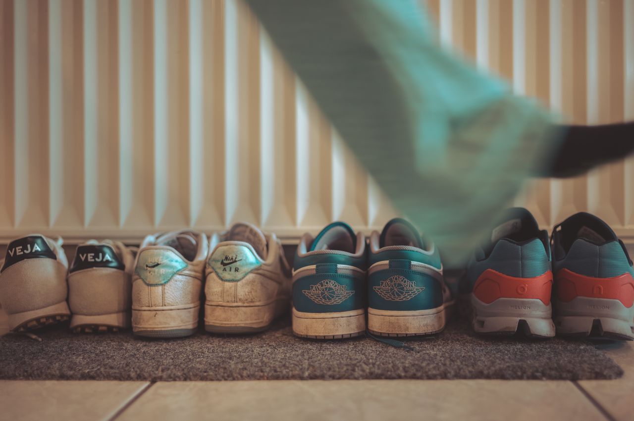 Four sets of sneakers in a row below a radiator.