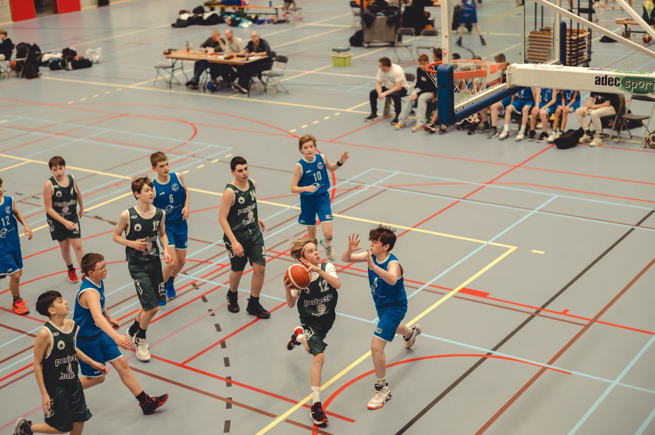 A teenage boy with a basketball runs towards the basket, while players from the other team try to catch him. He started his layup before they could reach him.