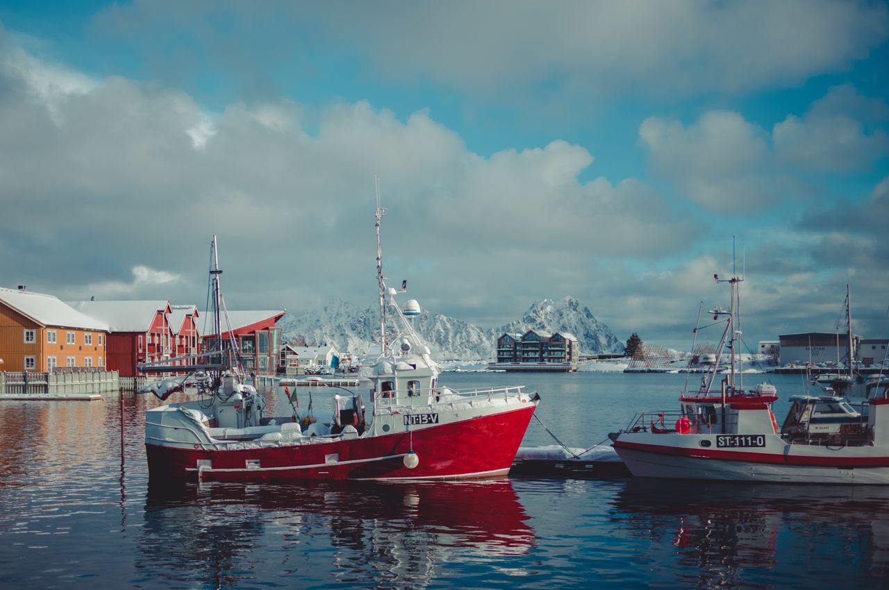 A small fishing boat docked on a jetty against the backdrop of a serene harbor.