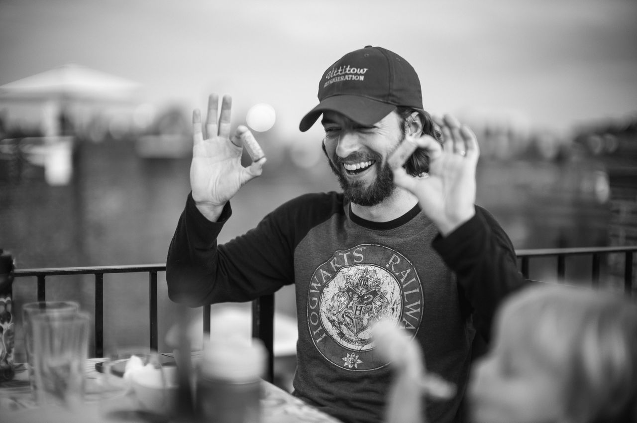 A person laughing, holding a cork in each hand after solving the party trick.
