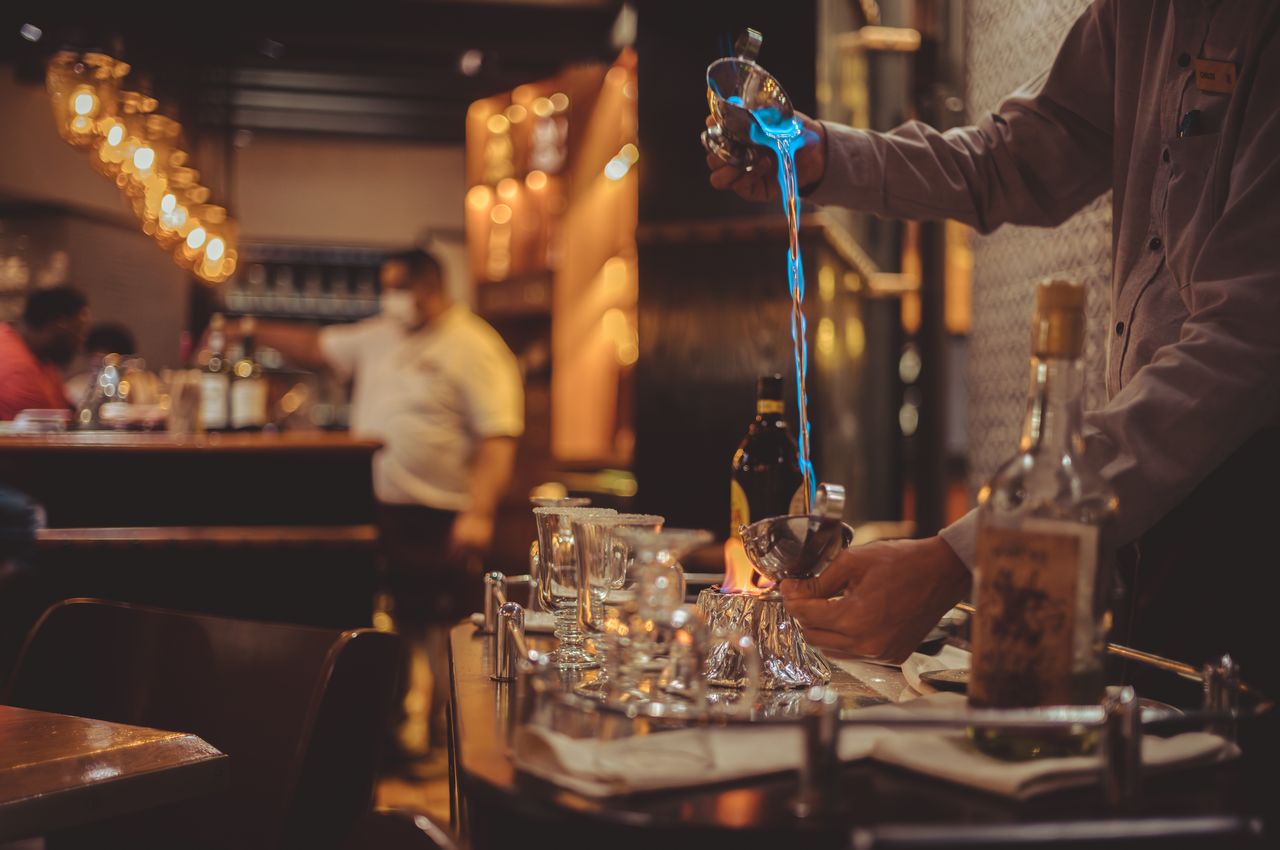 A bartender pours flaming liquid from one cup to another.