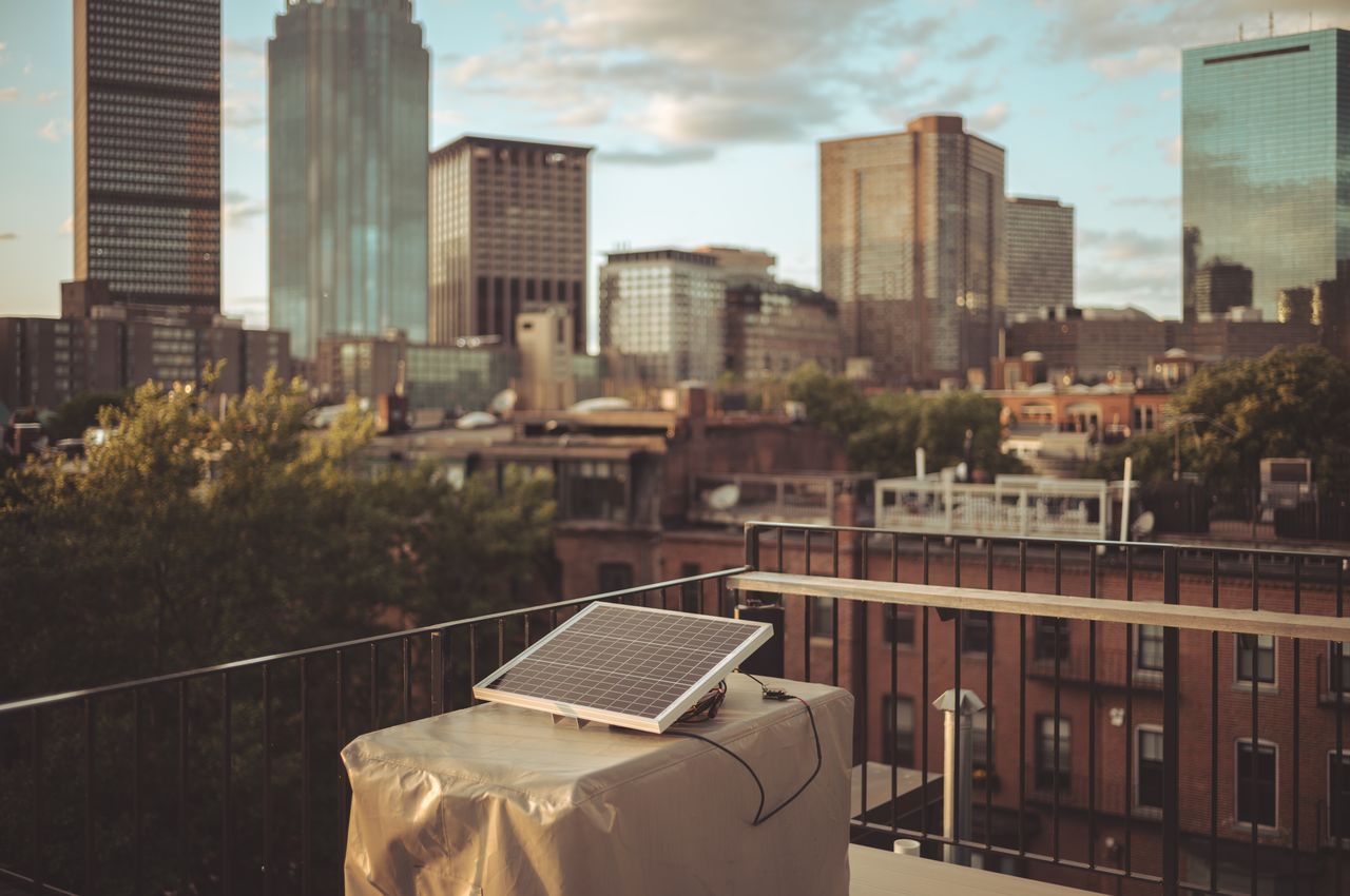 A solar panel on a rooftop during sunset with a city skyline in the background.
