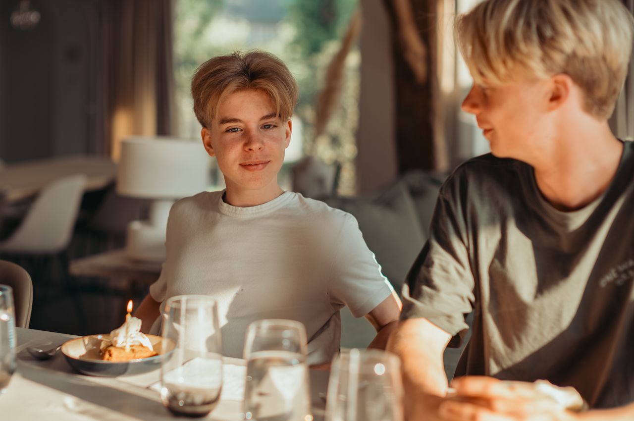 Two young men sitting at a kitchen island, one with a dessert that has a lit candle.