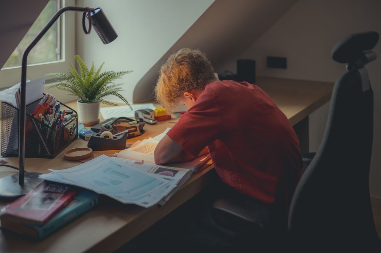 A young man siting at a desk, surrounded by study materials.